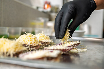 Chef adding grated parmesan to scallops au gratin in restaurant kitchen