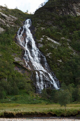 Waterfall cascading down a rocky cliff surrounded by lush greenery in a serene valley during daylight hours