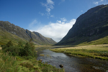 Scenic view of a river flowing through a valley surrounded by majestic mountains on a clear day in the countryside