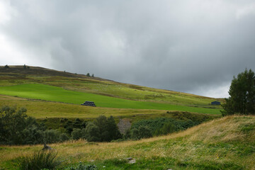 Rolling green hills under an overcast sky in a quiet countryside setting with patches of trees and farmland