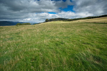 Expansive green field under a cloudy sky with distant mountains in the background during midday