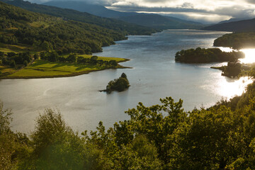 Scenic view of a tranquil lake surrounded by rolling hills and trees during golden hour in a serene landscape