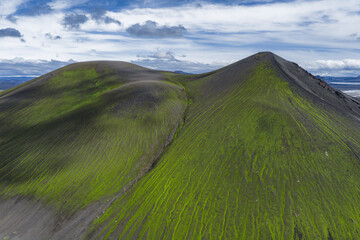 Two green moss covered volcanic hills in Iceland with streaks of vegetation and dark soil, set...