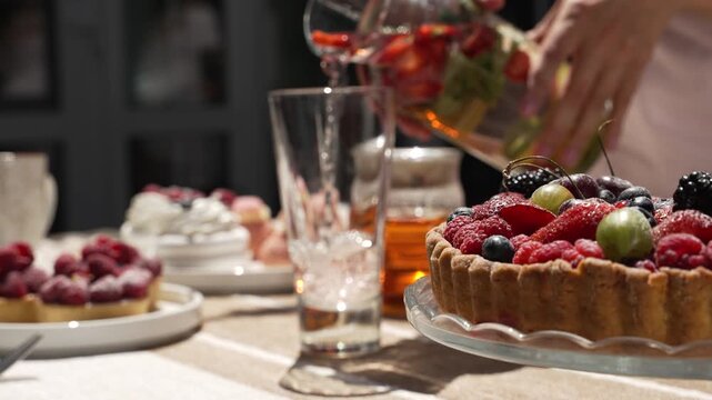 Berry desserts on the table in plates. Woman pouring lemonade with strawberries and raspberries into a transparent glass close-up in slow motion