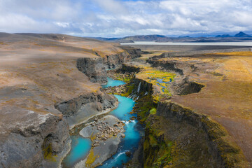 Sigoldugljufur Canyon, Iceland, features turquoise streams, cascading waterfalls, green moss, and rocky terrain under a partly cloudy sky.