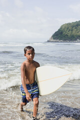 portrait of latin child boy with surfboard on the beach in Mexico Latin America, hispanic kid surfing in summer sport activity