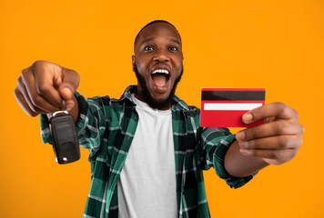 Make Dream Come True. African Man Showing New Car Key And Credit Card Buying Automobile Standing Over Yellow Studio Background. Auto Loan, Card-Based Payment Transaction And Banking Service