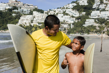 Latin father and son surfers holding surfboard on the beach in Acapulco Mexico. Hispanic people in summer sport activity