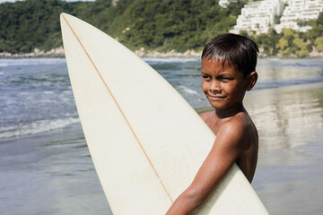 portrait of latin child boy with surfboard on the beach in Mexico Latin America, hispanic kid surfing in summer sport activity
