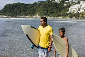 Latin father and son surfers holding surfboard on the beach in Acapulco Mexico. Hispanic people in summer sport activity