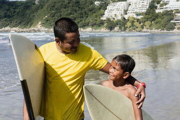 Latin father and son surfers holding surfboard on the beach in Acapulco Mexico. Hispanic people in summer sport activity