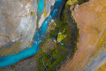 Turquoise river winds through moss covered Sigoldugljufur Canyon and earthy terrain in Iceland. Small waterfalls cascade into the river, creating dynamic movement.