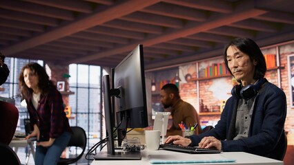 AI startup senior programmer overseeing deep learning application, thinking how to improve software. Asian artificial intelligence tech venture engineer using PC to fix code bugs, camera B