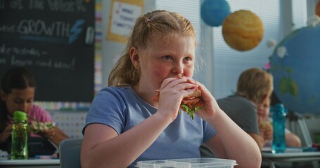 Young Girl Sitting at the Desk, Eating Yummy Homemade Sandwich from Lunch Box, Talking to Classmate...