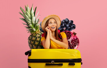 A joyful traveler wearing a straw hat and bright yellow shirt is sitting on a yellow suitcase.