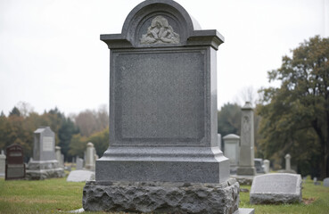 Fototapeta premium Granite headstone stands in quiet cemetery landscape. Solemn memorial features intricate carving at apex, with blank central panel ready for inscription. Gray stone surrounds peaceful resting place,