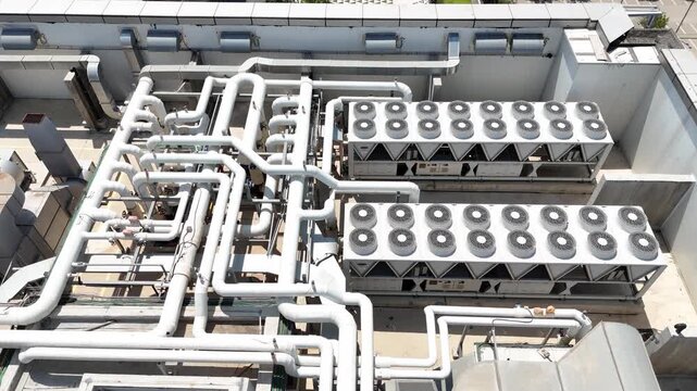 Aerial drone view of industrial HVAC systems, air conditioning units, ventilation fans, and piping on the rooftop 

