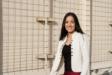 Smiling young latin businesswoman posing in front of metal grid wall