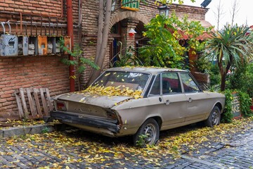 Abandoned car with autumn leaves on cobblestone street.