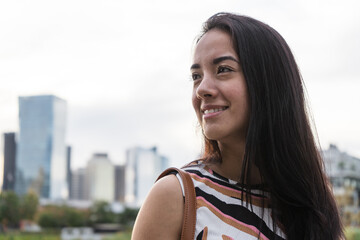 Young latin woman smiling and looking away in urban park with city in background