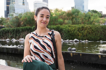 Young latin woman smiling in a city park with an artificial pond