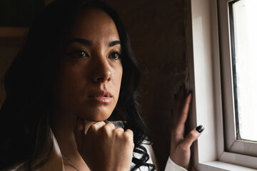 Pensive young woman looking out window in thoughtful pose