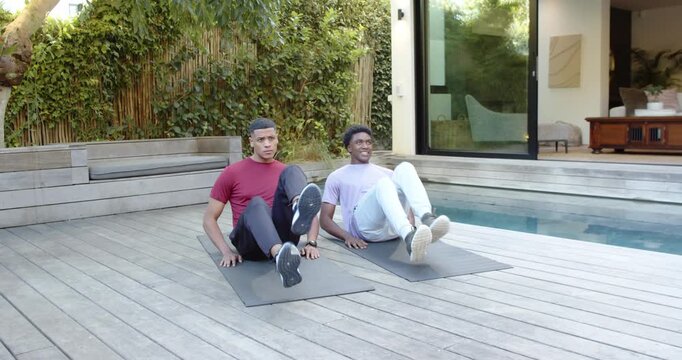 Completing flutter kicks on exercise mats, diverse male friends guiding breathing on deck by pool