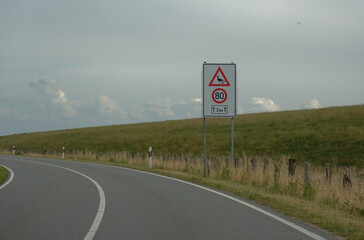 Curved Road with Falling Rocks Warning Sign near dagebuell at north sea next to a dike