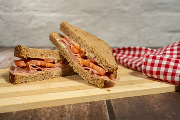 Two appetizing ham and tomato sandwiches resting on wooden cutting board