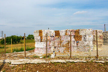 Large bales of recycled paper stacked neatly in a field, surrounded by a fence, showcasing sustainable waste management practices and environmental responsibility in a rural setting