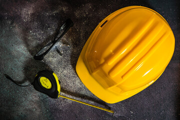 Yellow hard hat, measuring tape and safety glasses resting on dusty surface