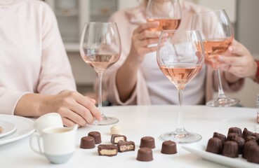 Friends share rose wine, gourmet chocolates in cosy home setting for relaxing evening. Indulgent sweet treats, drinks create delightful culinary experience for loved ones. Casual attire, pastel