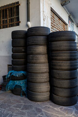 Stacked black tires in a A collection point for old car tires setting, showcasing various tread patterns and textures, surrounded by blue tarps and concrete flooring