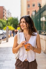Young woman enjoying a refreshing fruit juice while strolling through city streets.