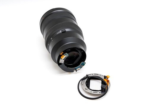 Broken camera lens with detached bayonet mount on white background.