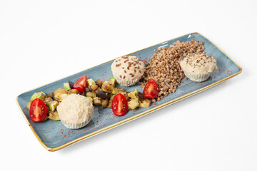 Top view of a healthy meal with steamed chicken meatballs, buckwheat, sautéed vegetables, and cherry tomatoes