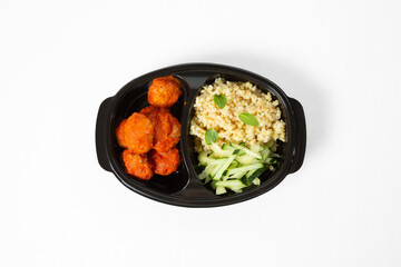 Bowl with bulgur, meatballs in tomato sauce, and fresh cucumber sticks on a white background. Top view