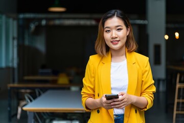 Smiling Young Woman in Yellow Blazer Using Smartphone in Modern Restaurant
