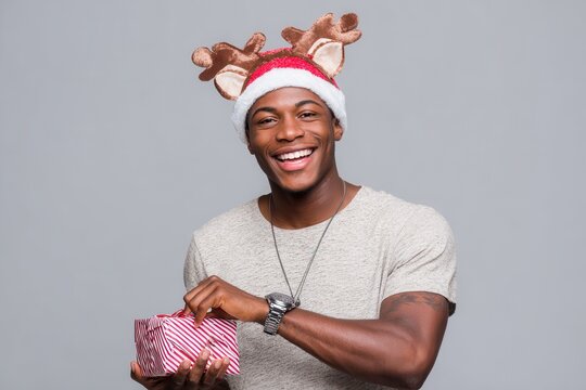 Relaxed and confident young Black man in a deer themed Christmas hat holding a gift and checking his watch