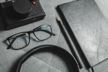 Notebook, pencil, headphones, glasses, camera, placed on a gray background.
