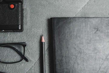 Notebook, pencil, headphones, glasses, camera, placed on a gray background.