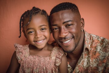 Smiling African American father and daughter pose together in front of a plain orange background, showing familial affection and happiness