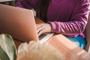 Young woman wearing a purple sweater using her computer for study at her desk. Remote work.