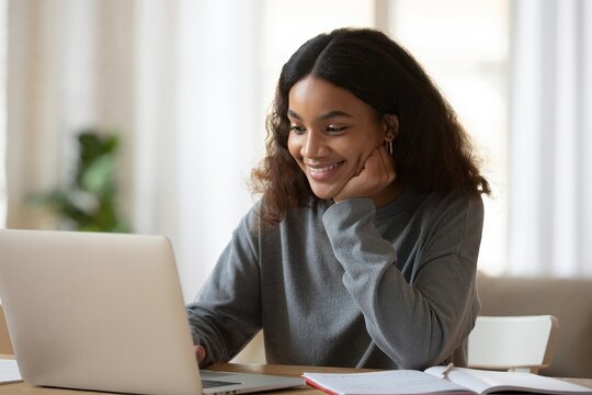 Smiling african american woman using laptop for online learning and video call home