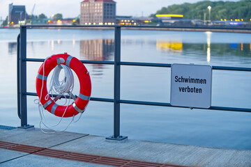 On Flensburg harbor promenade hangs a new clean lifebuoy and a sign with 