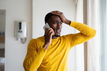 Stressed african american man talking on phone receiving bad news in yellow shirt indoors