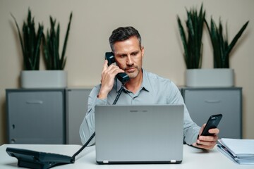 Man working at office desk with laptop, phone, and smartphone multitasking concept
