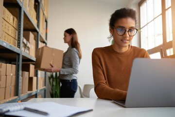 Ecommerce business owner working on laptop managing inventory in warehouse office