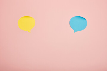 Yellow and blue paper speech bubble cutouts on pastel pink background, minimal abstract concept
