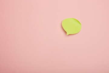 Green paper speech bubble cutout on pastel pink background, creative minimal design concept